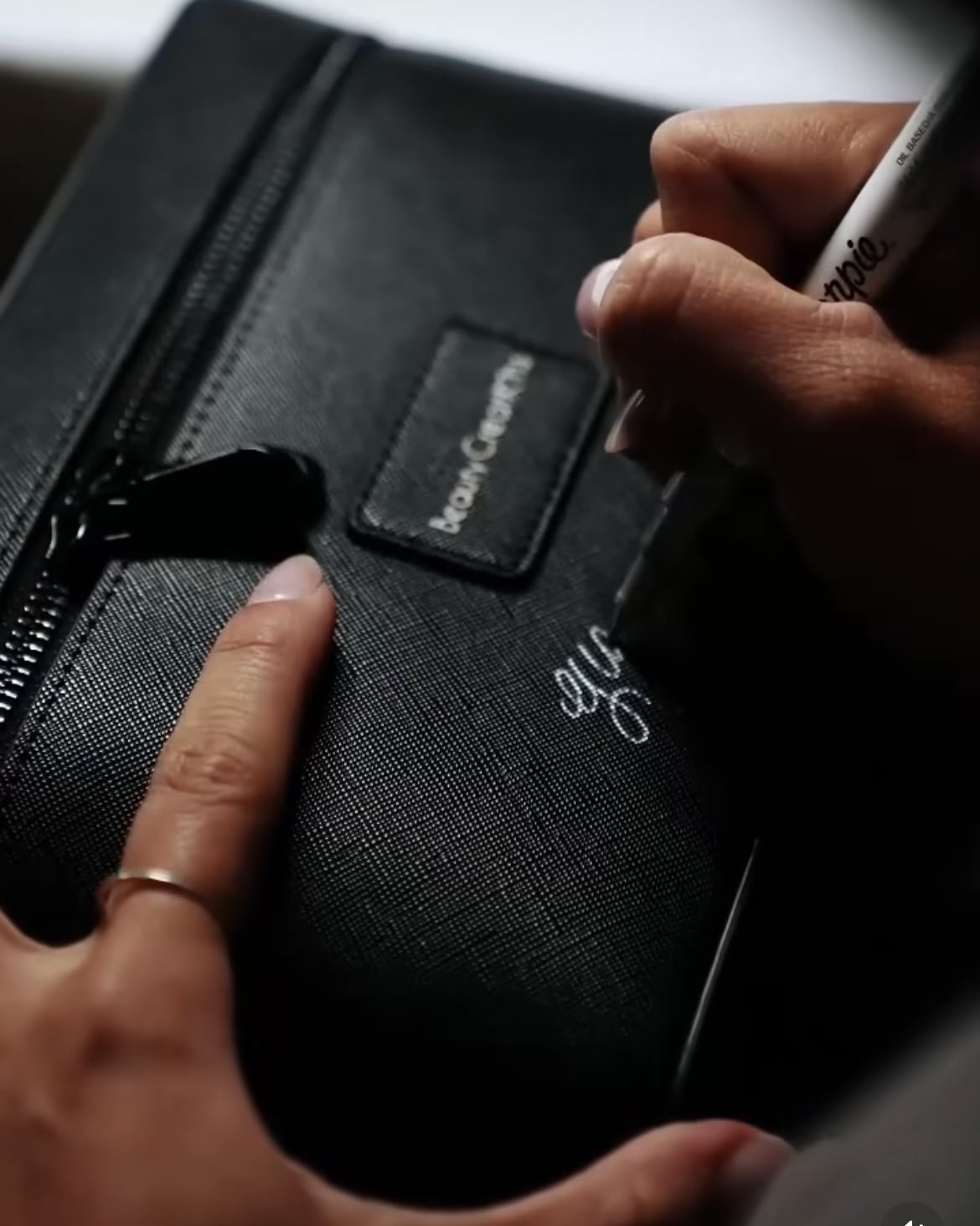 Close up of Cat Lauren Calligraphy customizing a cosmetic bag with calligraphy at a brand activation for Beauty Creations.