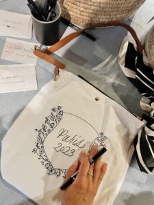 Close up shot of Cat Lauren Calligraphy personalizing tote bags at Hannah Godwin and Dylan Barbour's Welcome Cruise on the Seine River